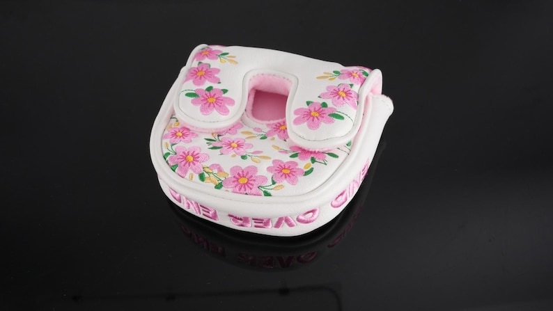 May include: A white mallet putter headcover featuring a pink floral pattern with green stems and leaves. The cover has a U-shaped opening and pink interior lining. The side of the white cover features the text "GAME OVER" embroidered in pink.