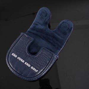 May include: A dark navy blue golf putter headcover featuring a textured crocodile skin pattern on the exterior and a soft fabric interior. The text END OVER END GOLF is printed in white on the front of the cover, which has a U-shaped opening.