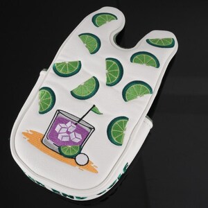 Pu&ograve; includere: Un copri bastone da golf bianco con un motivo ripetuto di fette di lime verde e una grafica di un cocktail viola in un bicchiere con cubetti di ghiaccio, una cannuccia nera e una fetta di lime, su un design a spruzzo arancione chiaro.