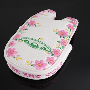 May include: A white golf putter headcover featuring a green bridge illustration and pink floral embroidery. The text "RIVER END GOLF" is embroidered in pink along the side edge. The cover has a U-shaped cutout at the top and a textured surface.