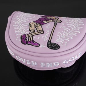 May include: A light purple golf putter cover with an embroidered cartoon golfer leaning on a golf club. The cover has white embroidered floral accents and the words "END OVER END GOLF" in white.