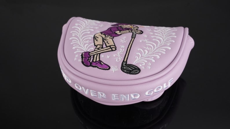 May include: A light purple golf putter cover with an embroidered cartoon golfer leaning on a golf club. The cover has white embroidered floral accents and the words "END OVER END GOLF" in white.
