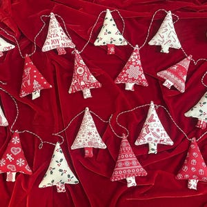 May include: A Christmas tree garland featuring fabric trees in red and white patterns. Some trees display festive text. The garland is strung on twine, ideal for seasonal decorations. Each tree is approximately 10 cm tall.