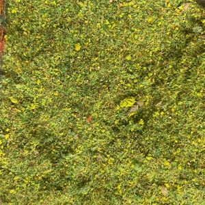 May include: Close-up of a patch of artificial grass, showcasing a vibrant mix of green and yellow hues. The texture appears dense and realistic, with small, yellow flower-like accents scattered throughout. The overall effect is a lush, natural appearance.