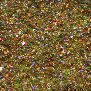 May include: A close-up view of a vibrant, textured surface. The surface is covered in a mix of green, red, yellow, white, and purple elements, resembling a miniature landscape or decorative material. The overall effect is colorful and detailed.