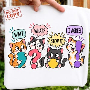Könnte beinhalten: Ein weißes T-Shirt mit einer bunten Grafik von vier Cartoon-Katzen und Sprechblasen. Die Katzen halten Satzzeichen: ein türkisfarbenes Komma, ein rosa Fragezeichen, einen gelben Kreis und ein violettes Ausrufezeichen. Text: WAIT, WHAT?, STOP IT., I AGREE!.