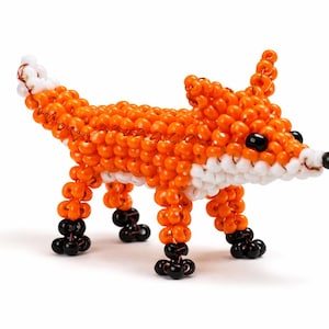 Peut inclure: Figurine de renard en perles. Le renard est principalement orange avec des détails blancs sur la queue et le museau. Les yeux sont noirs et les pieds sont noirs. Le renard est sur une surface blanche.