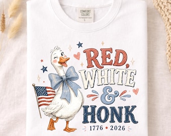 May include: A white t-shirt featuring a graphic of a winking goose wearing a blue bow, holding an American flag. The text reads RED, WHITE & HONK with the years 1776 and 2026 below. The design includes small stars and hearts in red and blue colors.