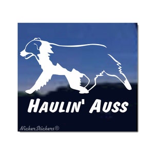 May include: White silhouette of an Australian Shepherd running with the text "Haulin' Auss" and the company name "Nicker Stickers" below.
