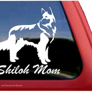 May include: White silhouette of a Shiloh Shepherd dog with the text "Shiloh Mom" below. The image is on a red car window.