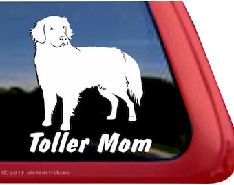 May include: White silhouette of a dog with the text "Toller Mom" below it. The dog is standing on its four legs with its head turned to the side. The image is on a red background.