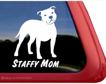 May include: White silhouette of a Staffordshire Bull Terrier dog with the text "Staffy Mom" below. The image is on a red car window.