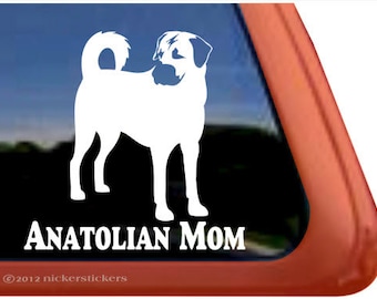May include: White Anatolian Shepherd dog sticker with the text "ANATOLIAN MOM". The sticker is a silhouette of the dog, and is displayed on a car window. The background shows a blue sky. The text is in a bold font.