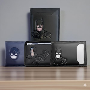 May include: A collection of superhero-themed wallets. The wallets are black and blue, featuring embossed designs of Batman, Captain America, and Cyborg. The wallets are displayed on a wooden surface.