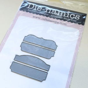 May include: A set of four silver-colored metal cutting dies for crafting, packaged in a clear plastic sleeve with a header card labeled Die-namics Exclusive Designs American Made Dies and the website address www.mftstamps.com printed on the top.