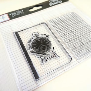 May include: Clear stamp set featuring a transparent stamp with a pocket watch design and the words "MONTHLY TIME BOOK". The set includes a grid stamp and is packaged on lined paper.