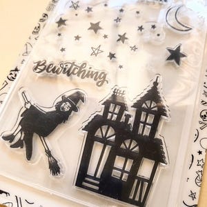 May include: Clear acrylic stamps featuring Halloween-themed designs. Includes a witch on a broom, a haunted house, stars, a crescent moon, and the phrases "Happy Halloween" and "Bewitching". Perfect for crafting and scrapbooking projects.