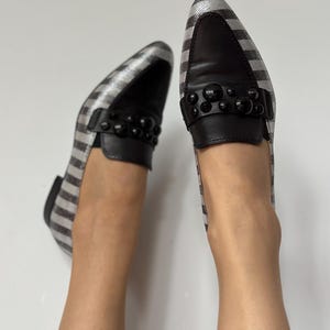 Peut inclure: Paire de mocassins &agrave; carreaux argent et noir avec des d&eacute;tails en cuir noir. Les chaussures ont un bout arrondi et une bride sur le dessus orn&eacute;e d'ornements sph&eacute;riques noirs. Fond blanc.