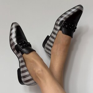 Peut inclure: Paire de mocassins ray&eacute;s argent et noir avec des d&eacute;tails en cuir noir. Les chaussures pr&eacute;sentent un design classique, un bout arrondi et une d&eacute;coration de perles noires sur le cou-de-pied.
