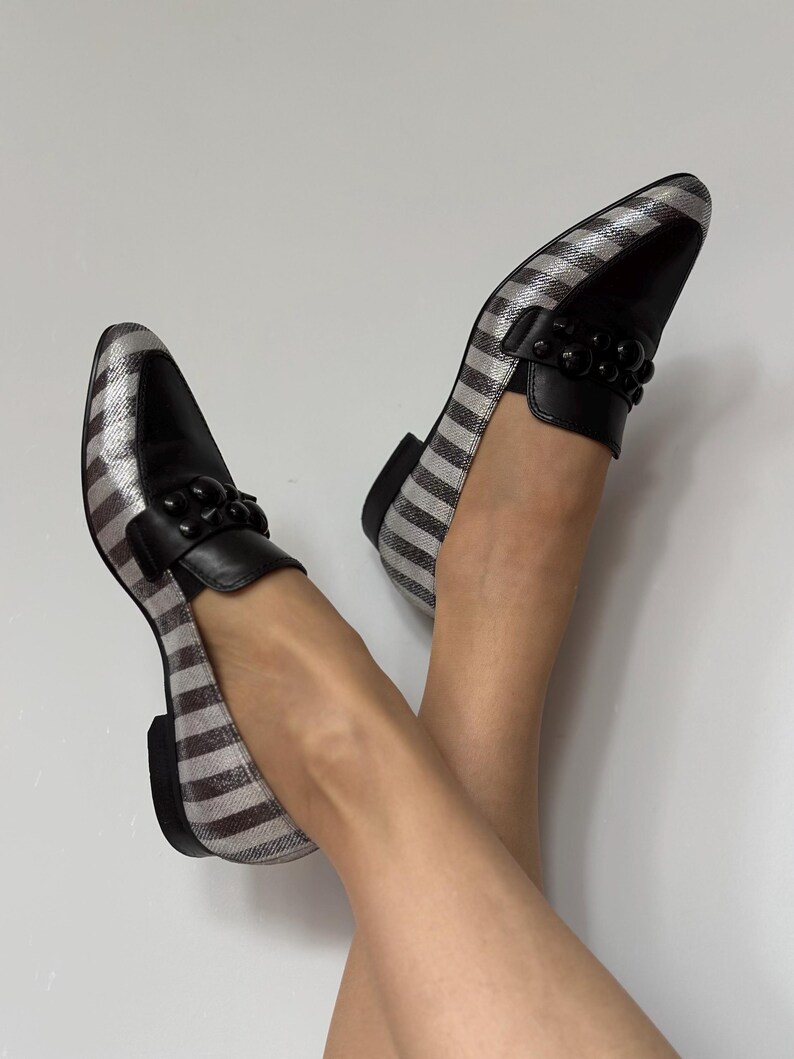 Peut inclure: Paire de mocassins ray&eacute;s argent et noir avec des d&eacute;tails en cuir noir. Les chaussures pr&eacute;sentent un design classique, un bout arrondi et une d&eacute;coration de perles noires sur le cou-de-pied.