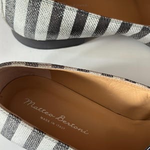 Peut inclure: Gros plan sur une paire de ballerines &agrave; rayures. Les chaussures pr&eacute;sentent un motif &agrave; rayures noires et blanches sur le dessus et une semelle noire. L'int&eacute;rieur de la chaussure est beige avec le texte "Matteo Bertoni MADE IN ITALY".