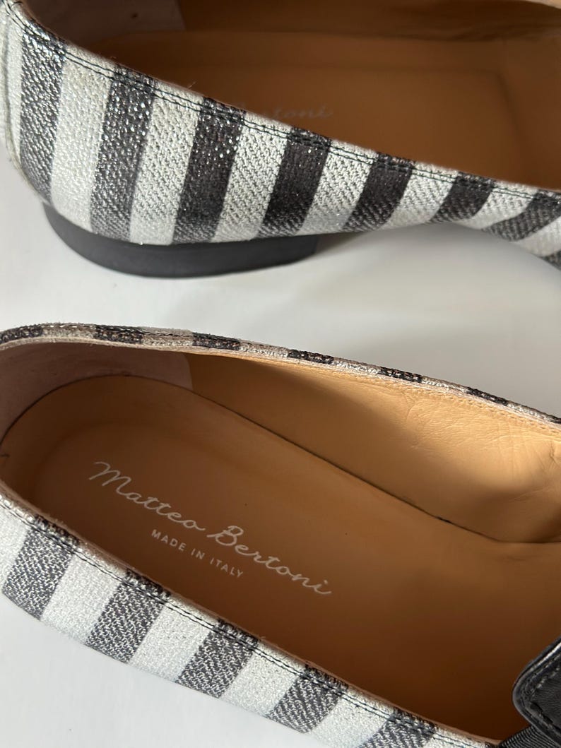 Peut inclure: Gros plan sur une paire de ballerines &agrave; rayures. Les chaussures pr&eacute;sentent un motif &agrave; rayures noires et blanches sur le dessus et une semelle noire. L'int&eacute;rieur de la chaussure est beige avec le texte "Matteo Bertoni MADE IN ITALY".