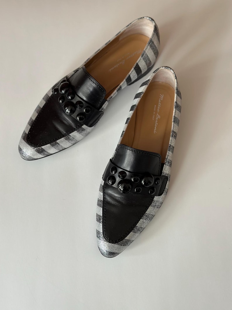 Peut inclure: Paire de mocassins ray&eacute;s noirs et argent&eacute;s avec des d&eacute;tails en cuir noir. Les chaussures ont un bout arrondi et une d&eacute;coration noire sur le cou-de-pied. L'int&eacute;rieur est de couleur beige clair.