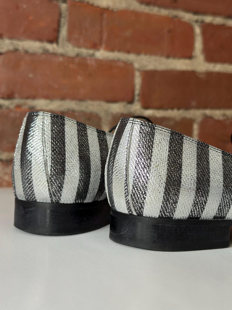 Peut inclure: Gros plan sur deux chaussures &agrave; rayures noires et argent&eacute;es. Les chaussures ont un petit talon et une semelle noire. Le motif ray&eacute; est vertical et recouvre l'ensemble de la tige de la chaussure.