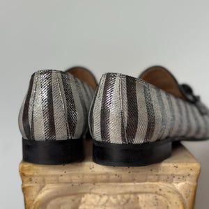 Peut inclure: Gros plan sur deux mocassins ray&eacute;s. Les chaussures pr&eacute;sentent des rayures verticales argent&eacute;es et noires. Les semelles sont noires et les chaussures sont pos&eacute;es sur une colonne d&eacute;corative.