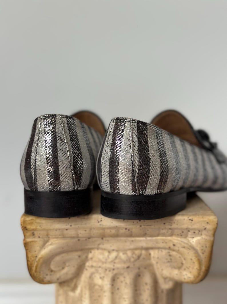 Peut inclure: Gros plan sur deux mocassins ray&eacute;s. Les chaussures pr&eacute;sentent des rayures verticales argent&eacute;es et noires. Les semelles sont noires et les chaussures sont pos&eacute;es sur une colonne d&eacute;corative.