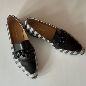 Peut inclure: Une paire de mocassins &agrave; rayures noires et blanches avec des d&eacute;tails en cuir noir. Les chaussures ont un bout arrondi et une d&eacute;coration sur le cou-de-pied. La marque "Matteo Bertoni" est visible sur la semelle int&eacute;rieure.