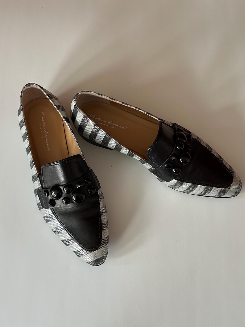 Peut inclure: Une paire de mocassins &agrave; rayures noires et blanches avec des d&eacute;tails en cuir noir. Les chaussures ont un bout arrondi et une d&eacute;coration sur le cou-de-pied. La marque "Matteo Bertoni" est visible sur la semelle int&eacute;rieure.