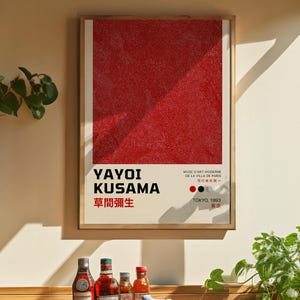 May include: A framed art print with a red dotted pattern and a diagonal design. The print displays the name "YAYOI KUSAMA" and Japanese text. Additional text indicates the museum and location, "TOKYO, 1993".