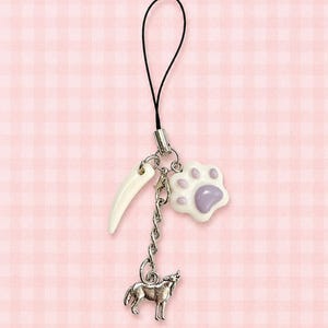 May include: A phone charm featuring a silver-toned metal chain with three dangling pendants: a white curved tusk-shaped charm, a white and light purple paw print charm, and a silver-toned metal wolf charm, all attached to a black cord loop.