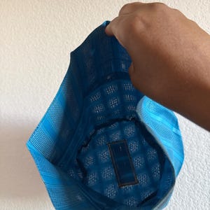 May include: A bright blue cap featuring a structured, grid-like woven texture. The headwear has a distinct geometric pattern throughout the fabric, with a rectangular patch visible on the interior lining of the crown, showcasing a mesh-like construction.