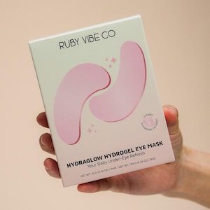 May include: A white box of Ruby Vibe Co Hydraglow Hydrogel Eye Masks. The box features pink eye mask illustrations and text that reads "Your Daily Under-Eye Refresh." The net weight is 0.35 oz per pair.