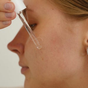 Model applying Ruby Vibe Co Gentle Savior Serum on cheek with dropper, calming hydration for smooth complexion.
