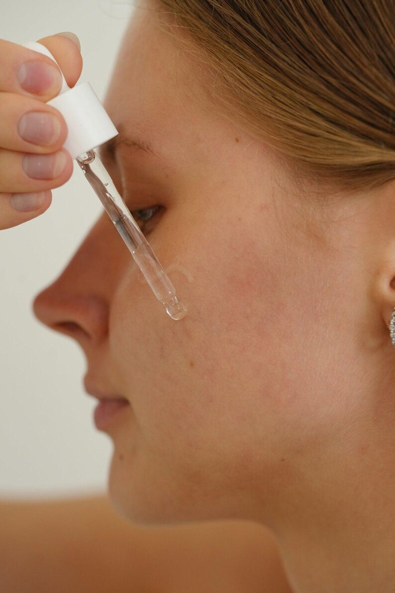Model applying Ruby Vibe Co Gentle Savior Serum on cheek with dropper, calming hydration for smooth complexion.