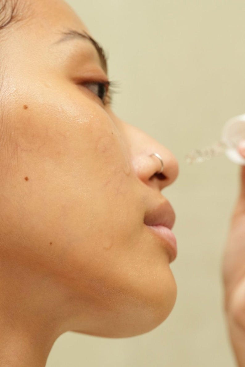 Model applying Ruby Vibe Co Radiant Boost Serum to cheek, lightweight texture absorbs quickly for dewy radiance.