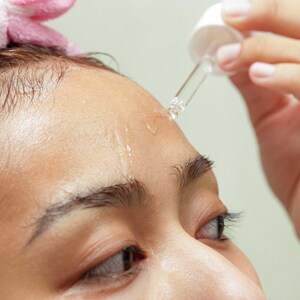 Close-up of model using dropper to apply Ruby Vibe Co Radiant Boost Serum on forehead, enhancing natural glow.