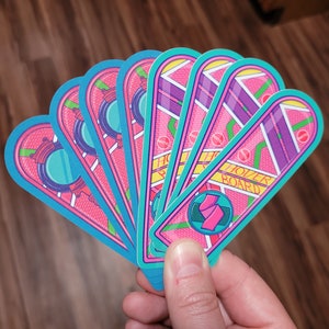 May include: A set of eight pink and blue hoverboard stickers with the text "Hoverboard" printed on one of the stickers. The stickers are designed to look like the hoverboard from the movie Back to the Future.