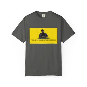 May include: Dark gray t-shirt featuring a yellow rectangle with a man and the text "TREAD IN THERE NICE & DEEP-LIKE". The graphic is centered on the front of the shirt. The shirt is made of a soft material.