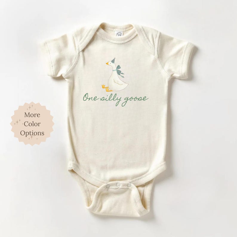 May include: Cream-colored baby onesie with a whimsical illustration of a goose wearing a party hat and bow. The text "One silly goose" is written in a script font. The onesie has short sleeves and snap closures.