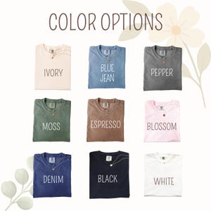 May include: Nine folded t-shirts in various colors, including ivory, blue jean, pepper, moss, espresso, blossom, denim, black, and white. Each shirt has a necklace and is labeled with its color name. The text "COLOR OPTIONS" is at the top.
