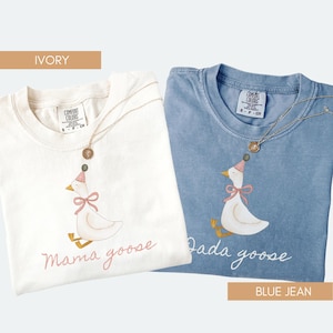 May include: Two t-shirts, one ivory and one blue jean, with goose illustrations. The ivory shirt has "Mama goose" text, and the blue jean shirt has "Dada goose" text. Both shirts have a gold necklace. The shirts are Comfort Colors brand.