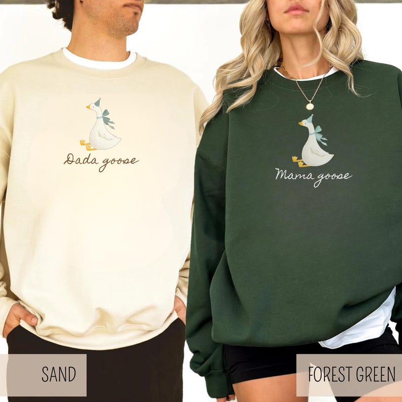 May include: Two sweatshirts, one sand-colored and one forest green, each featuring a goose graphic with a blue bow. The sand-colored sweatshirt has the text "Dada goose," while the forest green one says "Mama goose."