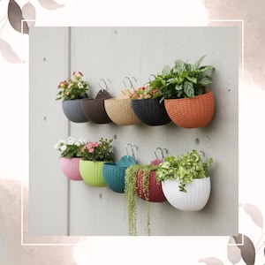 May include: A collection of colorful, wall-mounted hanging planters. Each planter, in shades like gray, brown, and orange, holds vibrant flowers and greenery. The planters are made of a woven material and are attached to a concrete wall with metal hooks.