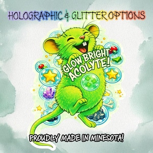 May include: A vibrant green cartoon mouse with a joyful expression, holding a sign that reads "GLOW BRIGHT ACOLYTE!" surrounded by bubbles with stars, crystals, and other elements. The text "HOLOGRAPHIC & GLITTER OPTIONS" and "PROUDLY MADE IN MINNESOTA!" are also visible.