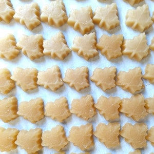 May include: A sheet of parchment paper with rows of maple leaf-shaped candies. The candies are a light brown color and have a slightly translucent appearance.