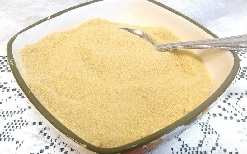 May include: A white ceramic bowl filled with light brown granulated sugar. A silver spoon rests on top of the sugar.